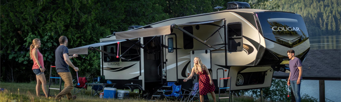 four people relaxing beside a Cougar fifth wheel